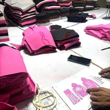 Apparel production table showing tech pack specifications, custom drawstring cords, and stacked cut fabric panels