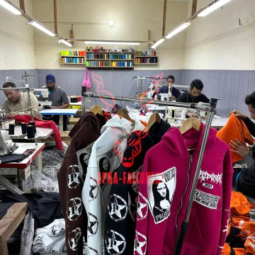 Custom heavy-fleece graphic full-zip hoodies hanging on a garment rack inside an active stitching factory facility